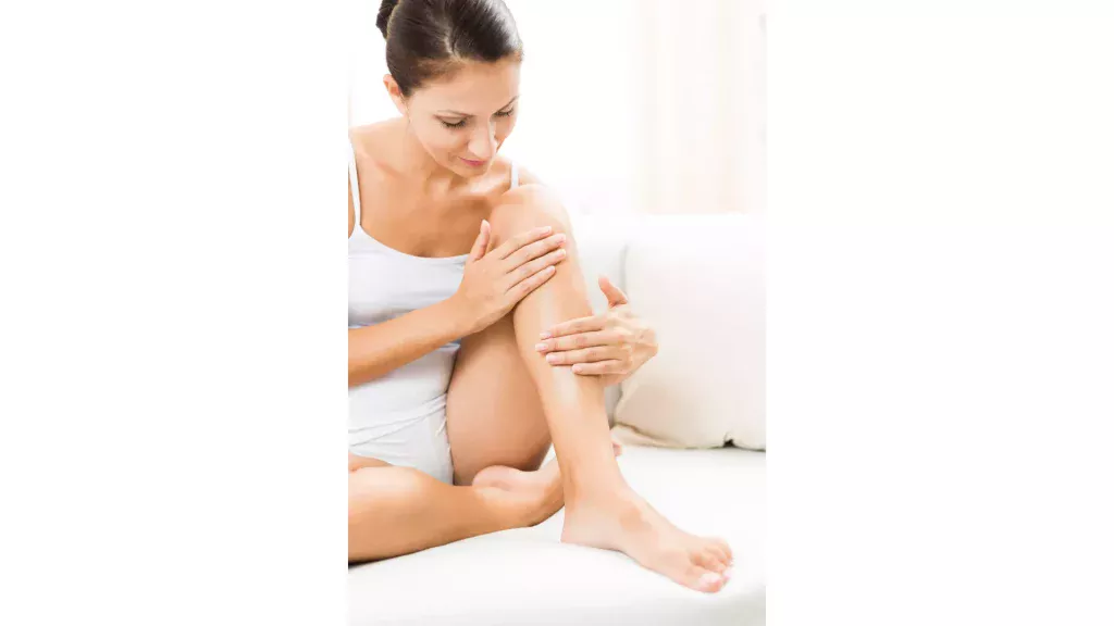 Une femme touche ses pieds pour montrer sa peau lisse et sans poils